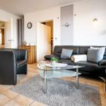 Wohnzimmer mit Ledersofa, Glas-Tisch und Teppich auf Fliesenboden.