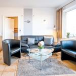 Wohnzimmer mit Ledersofa, zwei Sesseln und Glas-Tisch. Fenster mit Vorhängen und Teppich.