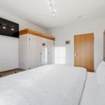 Schlafzimmer mit Bett, Kleiderschrank und Fernseher an der Wand.