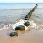 Wellen brechen an einer Reihe von grünen Steinen am Strand.