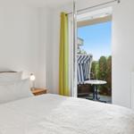 Schlafzimmer mit Blick auf Balkon mit Strandkorb und Tisch.