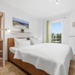 Schlafzimmer mit Bett, Regal und Fenster zum Garten.