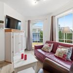 Wohnzimmer mit rotem Sofa, Fernseher und Fenster zur Terrasse.