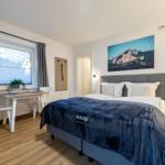 Schlafzimmer mit Bett, Schreibtisch und Fensterblick auf Berge.