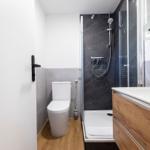 Badezimmer mit Dusche, Toilette und Waschbecken mit Holzschrank.