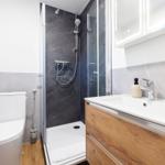 Badezimmer mit Dusche, Waschbecken und Toilette. Marmorfliesen und Holzschrank.