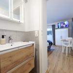 Badezimmer mit Waschbecken und Spiegelschrank. Im Hintergrund Schlafzimmer mit TV und Tisch.