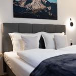 Schlafzimmer mit Bett, Kopfteil und Wandbild. Beleuchtung und Nachttisch sichtbar.