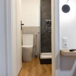 Badezimmer mit Dusche und Toilette, Holzboden und Nachttisch neben dem Bett.