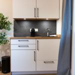 Küche mit weißen Schränken, Holzoberfläche und Pflanze an der Wand.