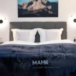 Doppelbett mit dunkelblauer Bettdecke und Bergbild an der Wand.