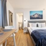 Schlafzimmer mit Doppelbett, Tisch, Fenster und Wandbild mit Bergmotiv.