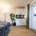 Zimmer mit Bett, kleiner Küchenzeile und Fenster mit Jalousie.