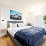 Schlafzimmer mit Doppelbett, Wandbild und Pflanze. Nebenraum mit Toilette und Dusche.