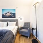 Schlafzimmer mit Bett, Sessel und Wandbild. Holzboden und Pflanze sichtbar.