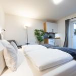 Schlafzimmer mit Doppelbett, Küchenzeile und Fenster mit Jalousie.