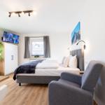 Schlafzimmer mit Bett, Sessel und TV. Fenster mit Vorhängen. Wandbild und Pflanze.