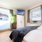 Schlafzimmer mit Bett, TV und zwei Fenstern mit Blick auf die Umgebung.