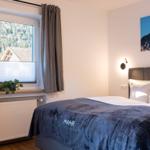 Schlafzimmer mit Bett, Fenster und Wandbild. Blick auf Wald und Haus.