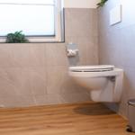 WC mit Wandmontage, Holzboden und Fenster mit Jalousie.