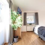 Schlafzimmer mit Bett, Fenster und Zimmerpflanze. Holzboden und Blick auf die Berge.