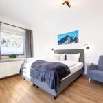 Ein Schlafzimmer mit Bett, Sessel und Fensterblick auf Berge.