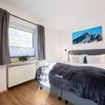 Schlafzimmer mit Bett, Fenster und Wandbild. Holzboden und graue Vorhänge.