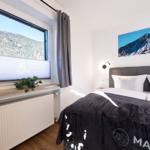 Schlafzimmer mit Bett, Fenster und Wandbild. Blick auf bewaldete Berge.