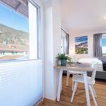 Zimmer mit Blick auf Berge, Tisch und Bett. Fenster mit Jalousie und Wandbild.