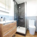 Badezimmer mit Dusche, Waschbecken und Toilette. Holzoptik und graue Fliesen.