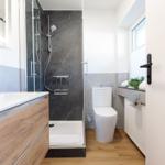 Badezimmer mit Dusche, Waschbecken und Toilette. Holzboden und graue Fliesen.