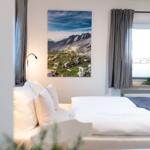 Schlafzimmer mit Bett, Wandbild und Fenster mit Vorhängen.