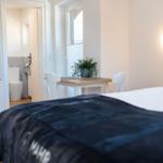 Schlafzimmer mit Bett, Tisch und Stühlen. Im Hintergrund ist die Toilette sichtbar.