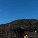 Haus mit Dach und Blick auf bewaldeten Berg unter blauem Himmel.