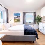 Schlafzimmer mit Bett, Fenster und Küchenbereich. Wandbild zeigt Berglandschaft.