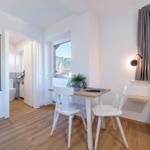 Zimmer mit Tisch, Stühlen, Bett und Bad. Fenster mit Blick auf Wald.