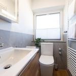 Badezimmer mit Waschbecken, Toilette und Heizung. Fenster mit Jalousie und Pflanze.