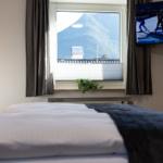 Ein Bett mit Blick auf einen Berg. Ein Fernseher zeigt eine Wintersportveranstaltung.