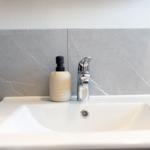 Waschbecken mit Wasserhahn und Seifenspender an grauer Wand