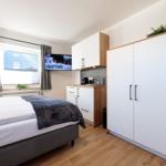 Schlafzimmer mit Bett, Kleiderschrank und Küchenzeile. Fenster mit Blick auf Berge.