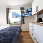 Schlafzimmer mit Bett, Fenster und Küchenzeile mit TV.