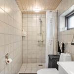 Bathroom with shower, toilet, and sink. White tiles and wooden ceiling.