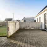 Backyard with paved area and wooden fence. Grass area beside the house.