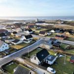 Aerial view of coastal village with houses, roads, and ocean in background.