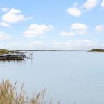 Boat is moored at the edge of a lake under a blue sky with white clouds.