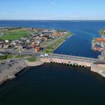 Aerial view of a coastal town with harbor, bridge, and wind turbines in the distance.