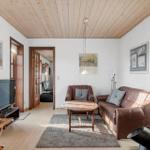 Living room with brown leather sofa, fireplace, and wooden ceiling. TV and table are present.