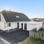 House with black roof and white siding, surrounded by lawn and fence.