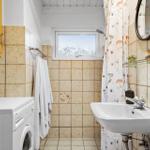 Badezimmer mit Waschmaschine, Spiegel und Duschvorhang mit Blumenmuster.