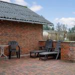 Terrasse mit zwei Liegestühlen, Tisch und Stuhl vor Backsteinhaus mit Garten.